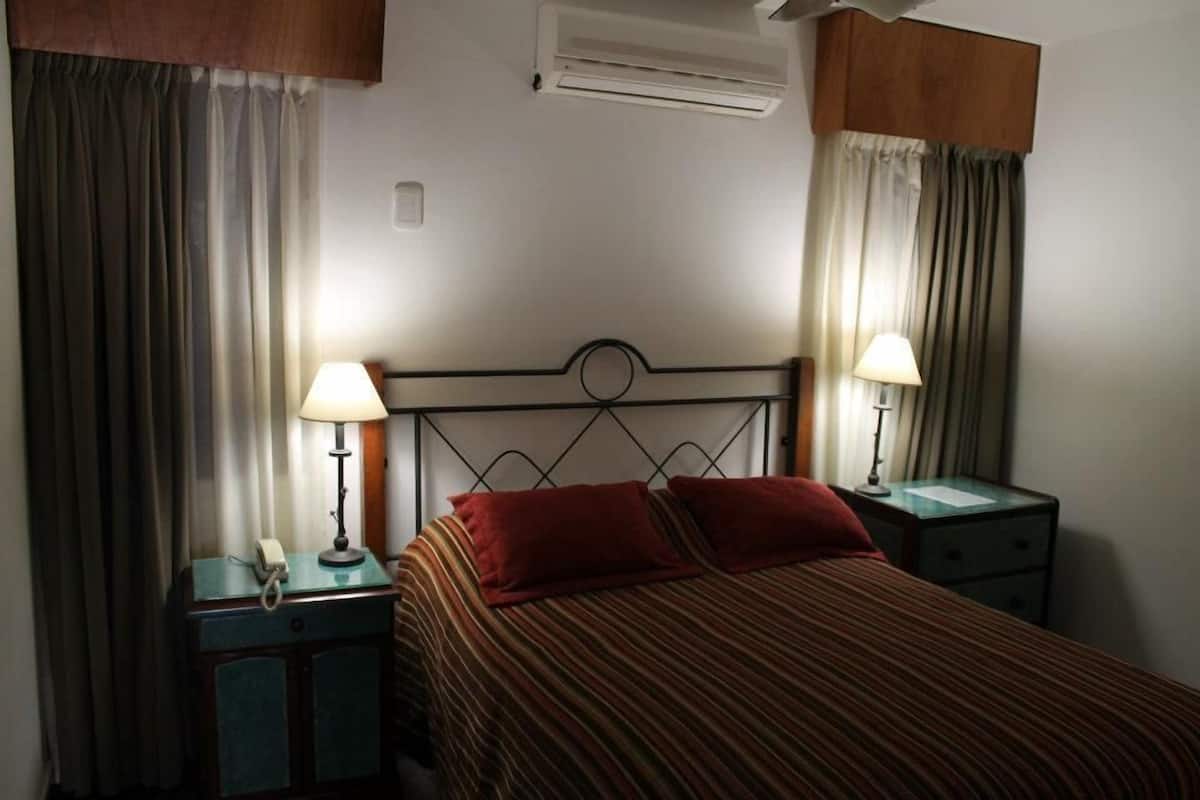 Ein Hotelzimmer mit einem Bett, zwei Nachttischen mit Lampen, einem Telefon und Vorhängen.