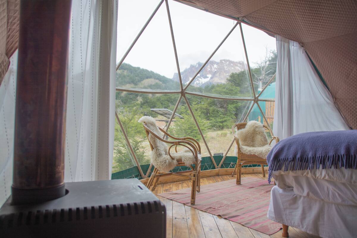 Una habitación acogedora con cama, una silla y vistas a un paisaje montañoso a través de un ventanal.