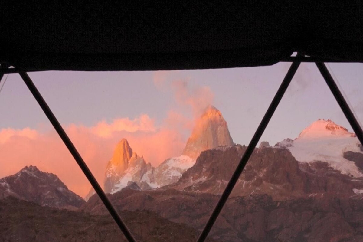 Un paysage de montagne vu à travers une fenêtre ornée d’une grille métallique.