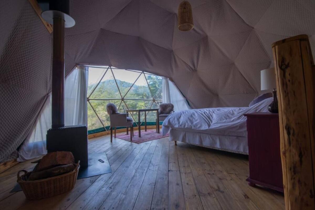 Alojamiento en tienda de campaña acogedor, con cama, mesa y vistas al exterior.