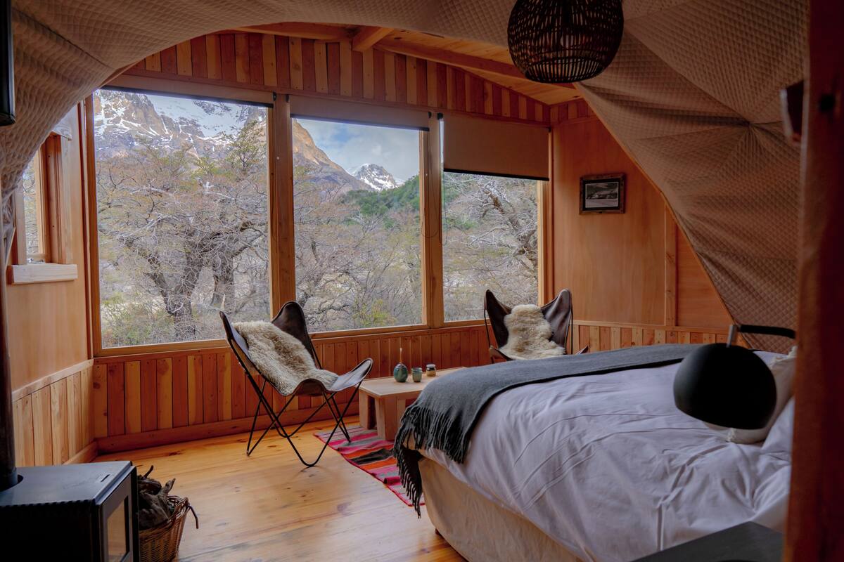 Un dormitorio acogedor con una ventana grande, una cama, una silla y una mesita.
