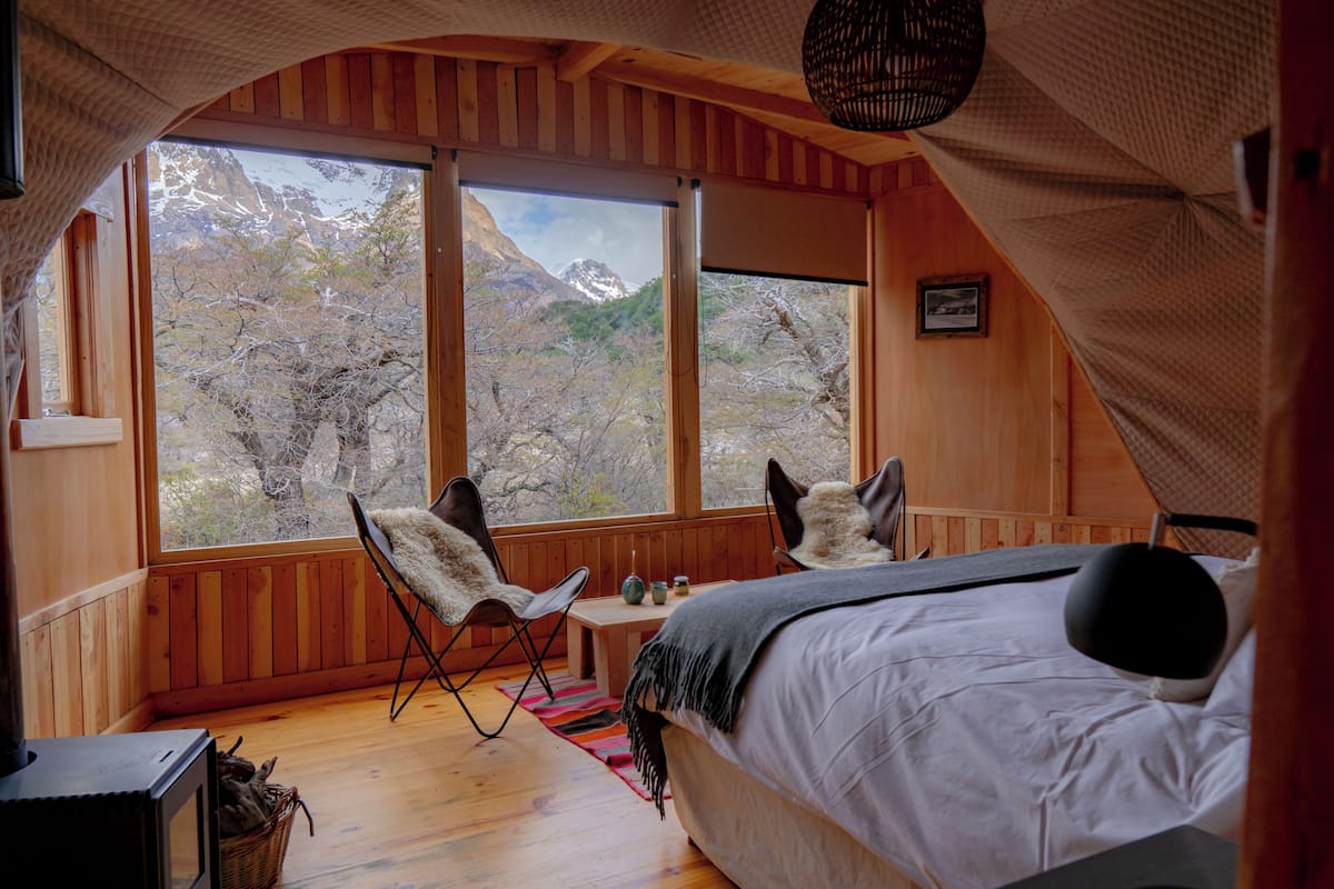 A cozy bedroom with a large window, a bed, a chair, and a small table.