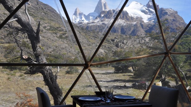 Un comedor con una mesa lista para dos personas, con vistas a un paisaje montañoso de picos nevados.