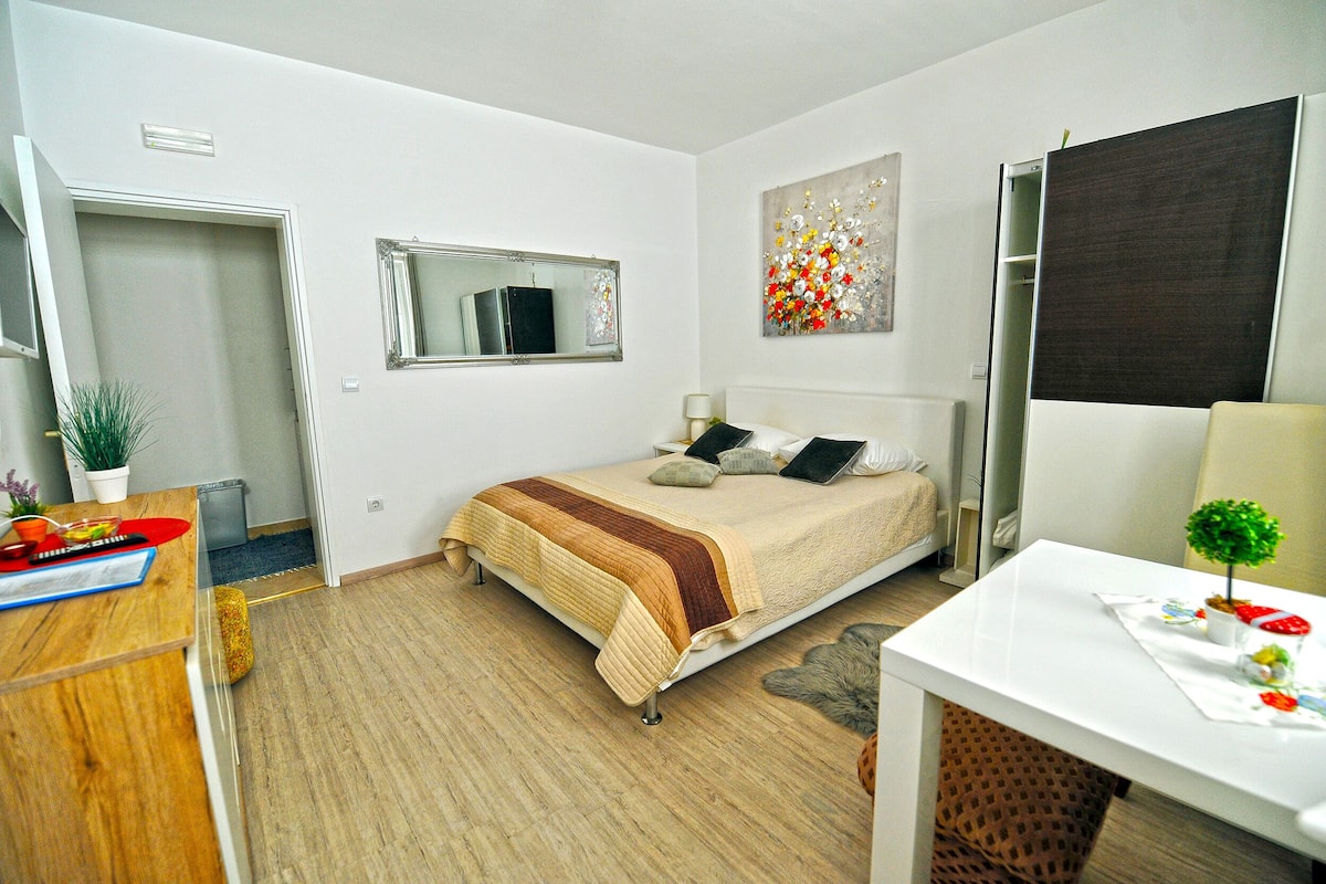 Quarto com cama, escrivaninha, cadeira, espelho e uma pequena planta.