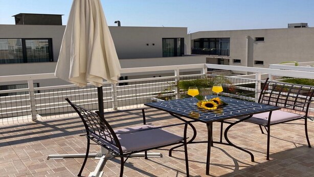 Terraço no telhado com mesa, cadeiras, guarda-sol e vista para edifícios modernos.
