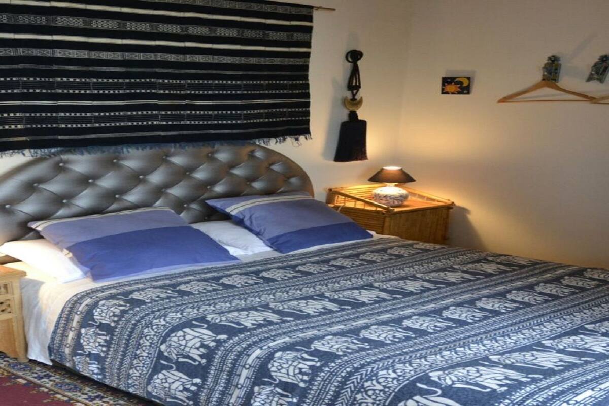 A bedroom with a tufted headboard, patterned bedspread, bedside lamps, and a small wooden nightstand.