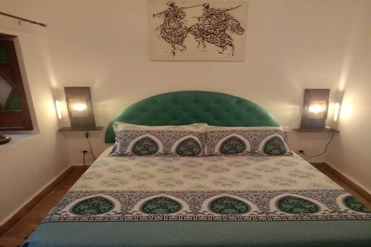 A bed with a green upholstered headboard, patterned bedding, and two wall-mounted lamps.