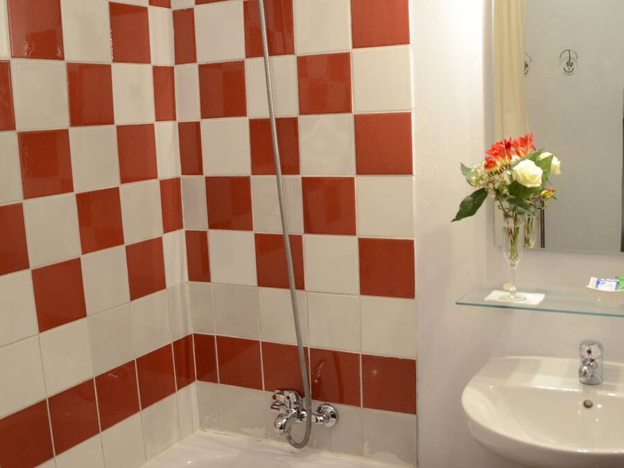 A bathroom with a checkered red and white tile wall, a white bathtub, a glass shelf with a vase of flowers, and a sink with a mirror above it.