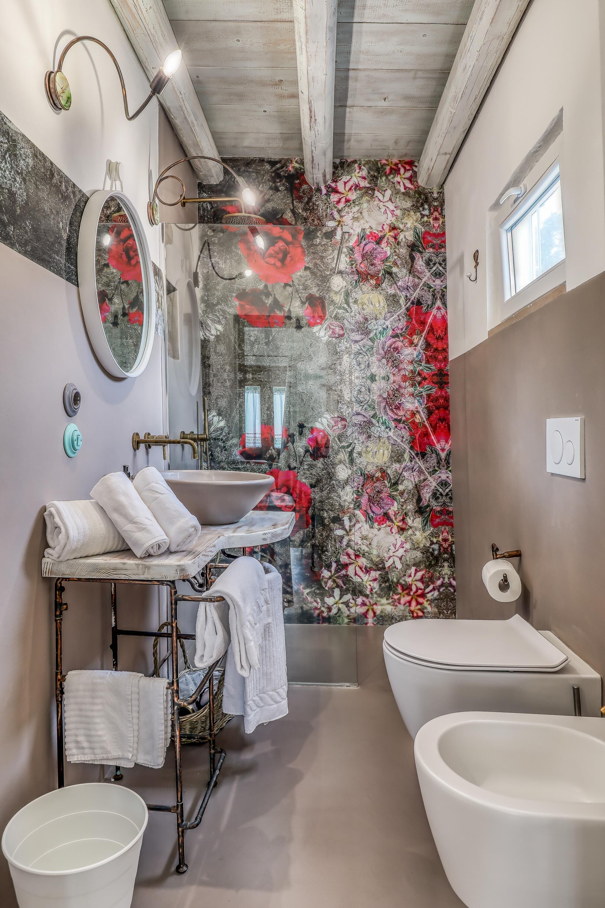 Ein Badezimmer mit einer großen Badewanne, einem Waschbecken inklusive Spiegel und einer Wand mit floralem Wandpapier.