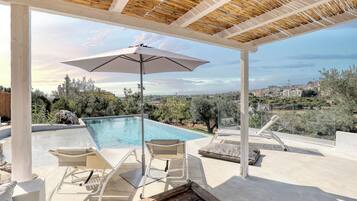Un espacio al aire libre techado con piscina, sillas de descanso y una sombrilla.