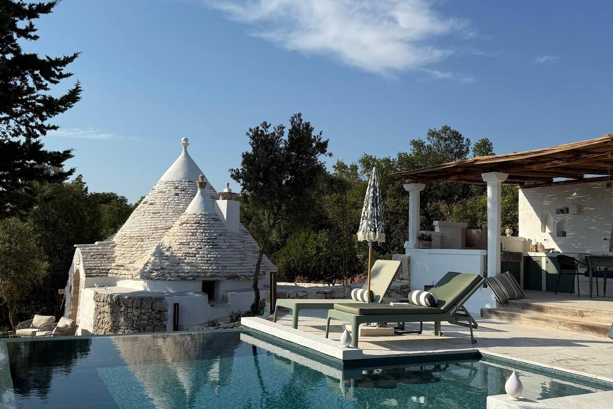 Un espace piscine comprenant des chaises longues, une structure en pierre et une pergola.