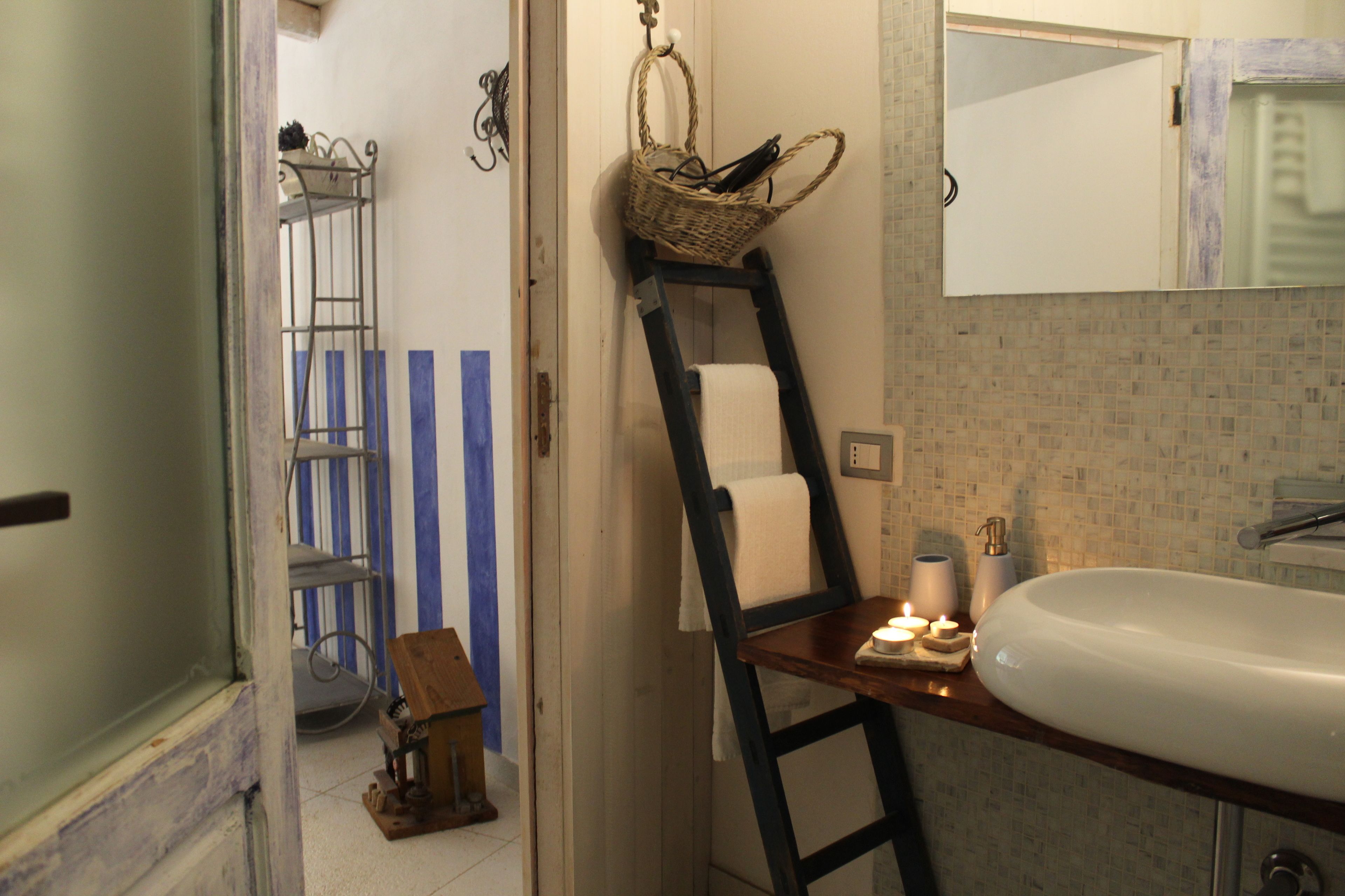 A bathroom with a wooden ladder, a white sink, a mirror, and a basket hanging on the wall.