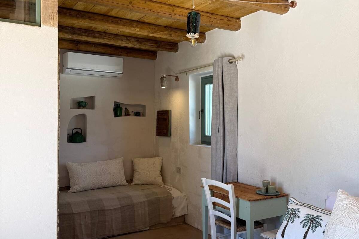 Une chambre avec un plafond en bois, un lit recouvert d’une couette blanche, une petite table avec une chaise et une fenêtre avec des rideaux.