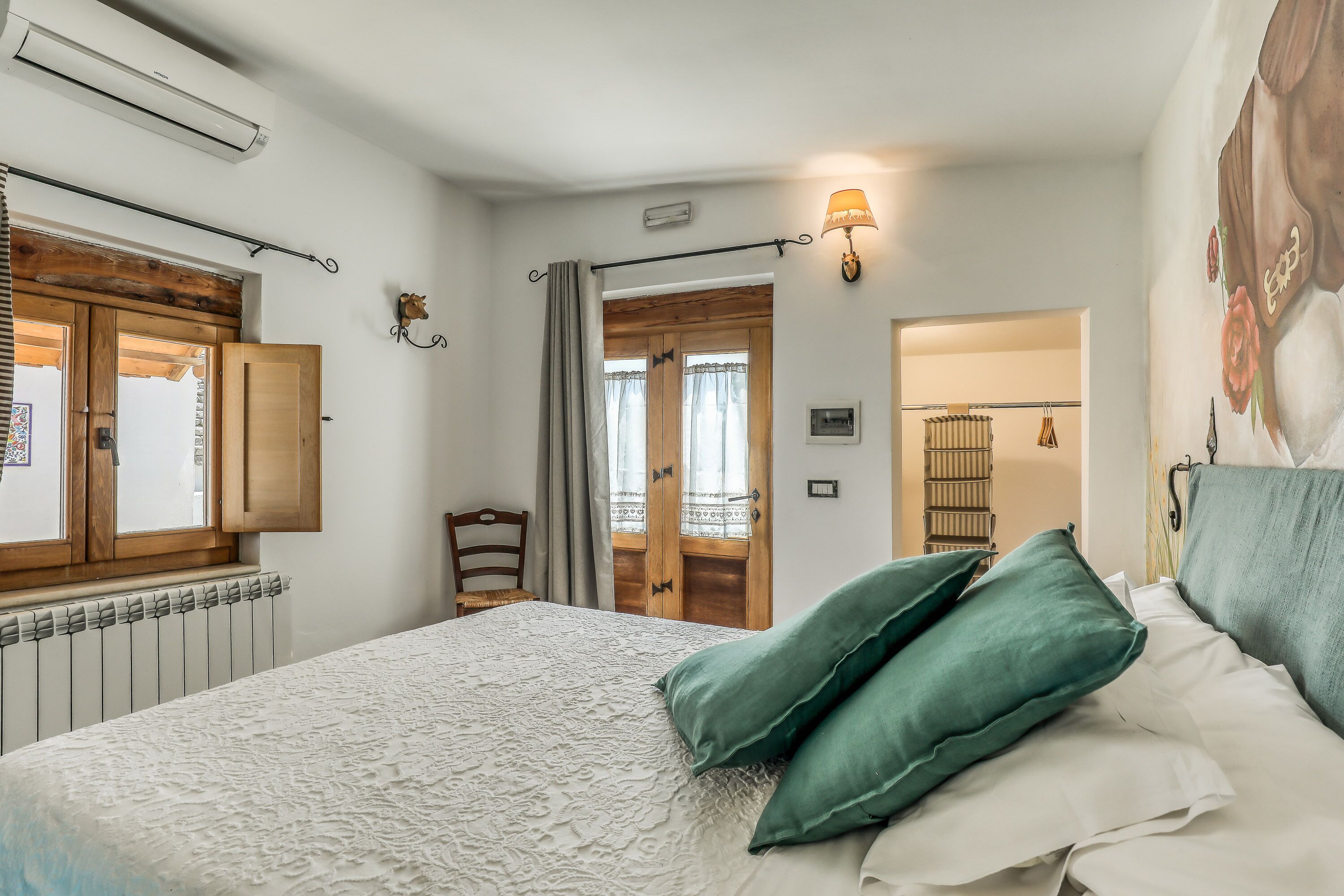 A bedroom with a bed, a radiator, a wooden door, a chair, and a wall-mounted light fixture.