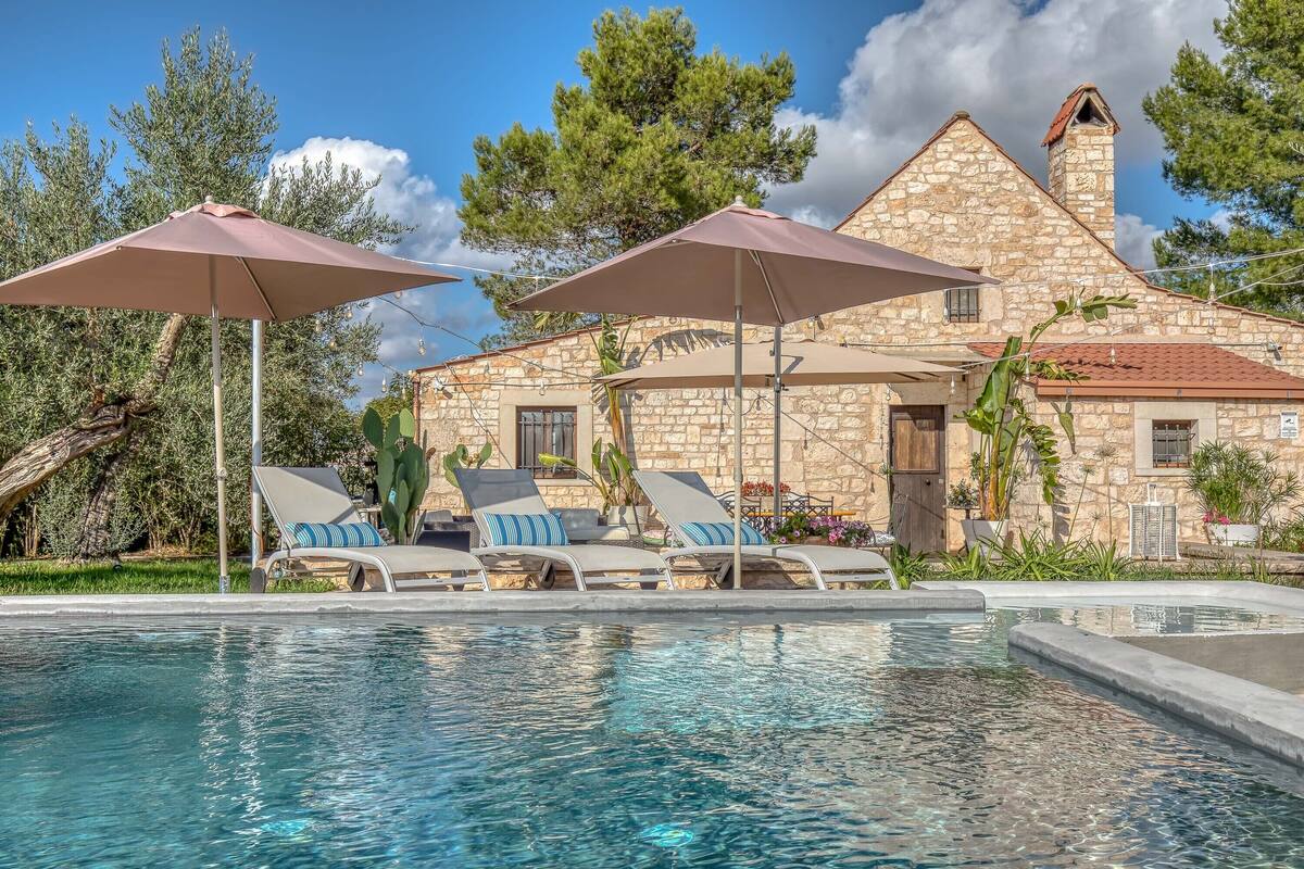 Un bâtiment en pierre doté d’une piscine, de chaises longues et de parasols.