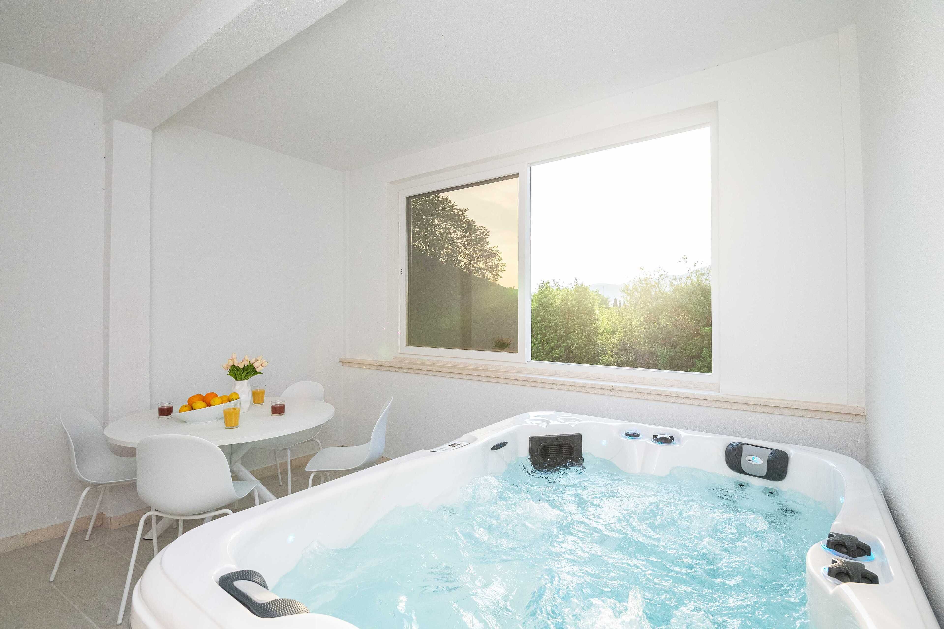 Quarto com hidromassagem, mesa de jantar com cadeiras e janela com vista para o verde.