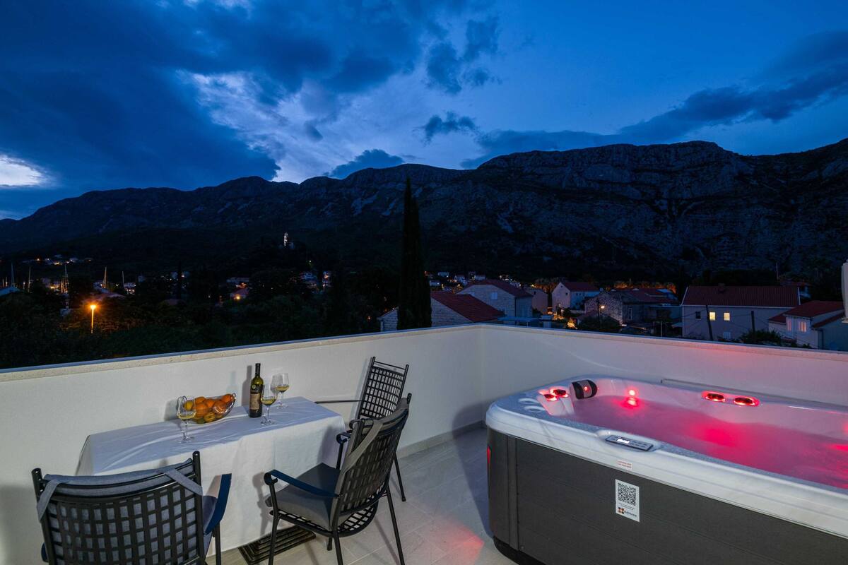 A balcony with a table set for two, a hot tub, and a mountain view.