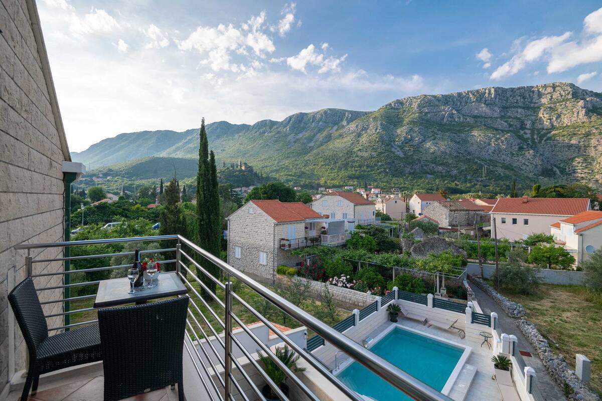A balcony with a pool, stone houses, and mountains in the background.