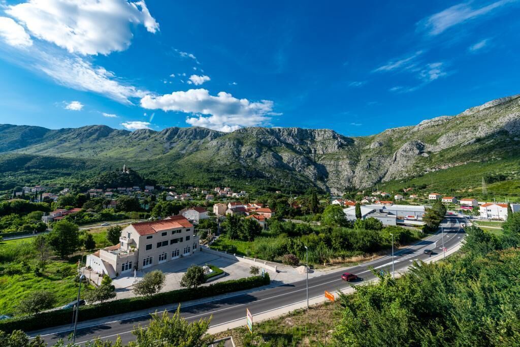 A town with a prominent building featuring a red roof, surrounded by lush greenery and mountains in the background.