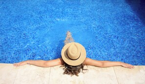 Une personne allongée sur le bord d’une piscine, les bras tendus.