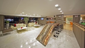 A modern hotel lobby with a marble floor, a central bar area, and seating arrangements.