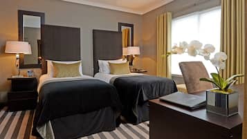 Ein Hotelzimmer mit zwei Betten, einem Schreibtisch, einem Sessel und einem großen Fenster mit Vorhängen.