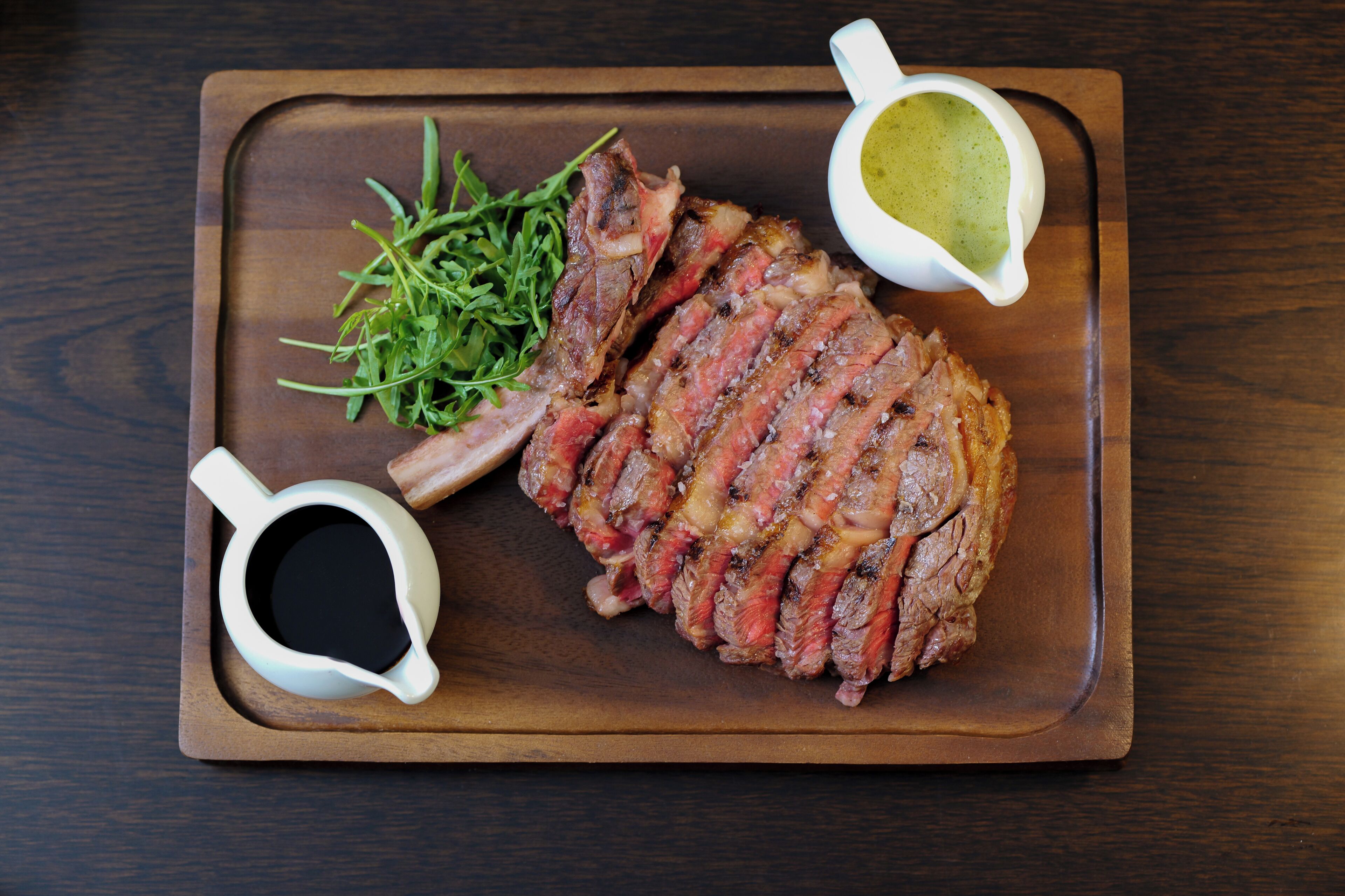 A steak with two sauces on a wooden board.