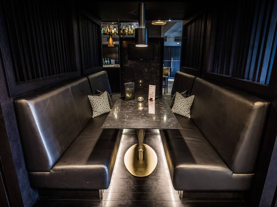 A dark-themed restaurant with booth seating, a marble table, and a bar area in the background.
