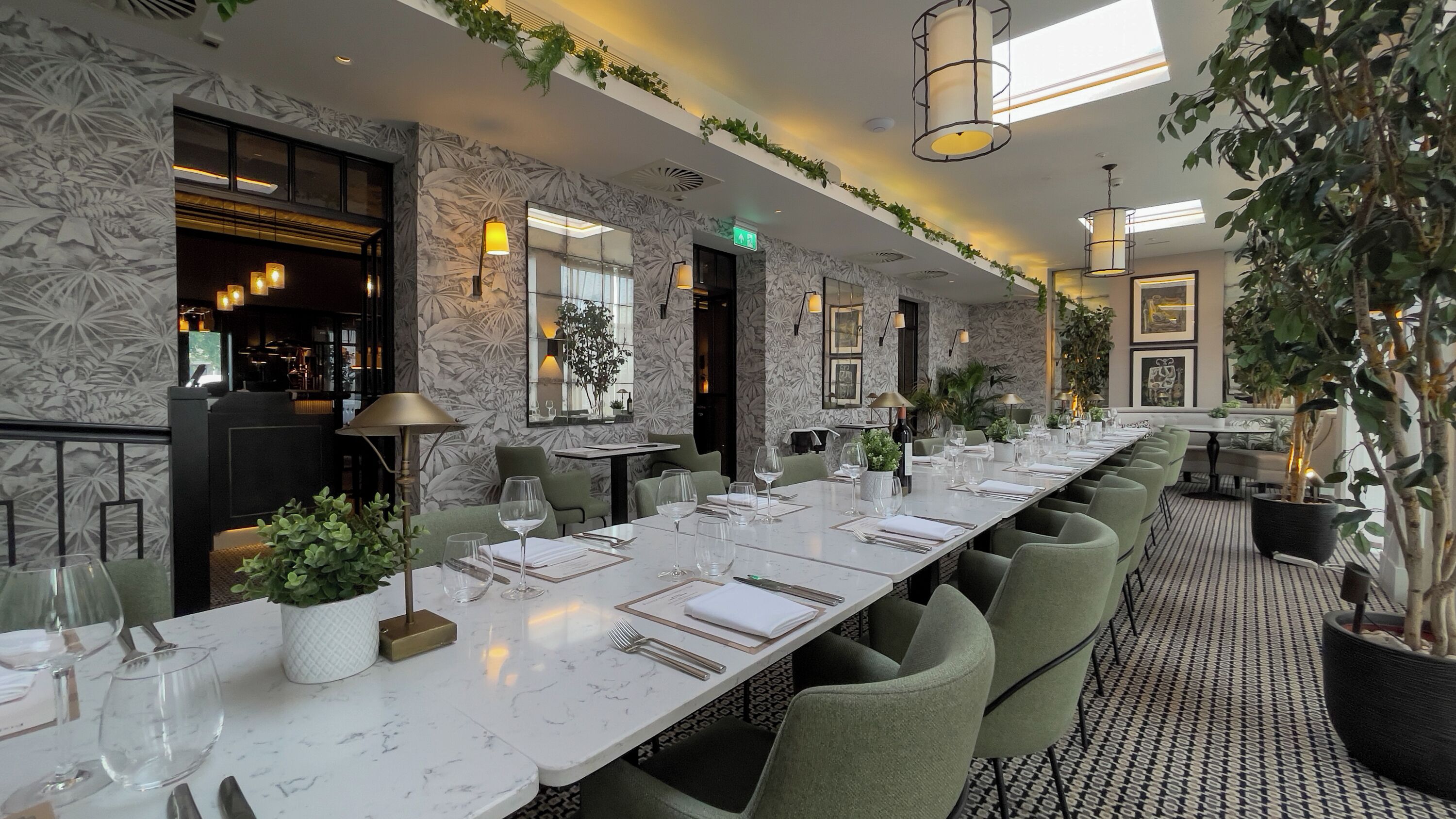 A long dining table set with chairs, a bar area, and decorative plants.