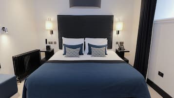 Habitación de hotel con una cama grande, dos lámparas de noche, cabecero negro y un radiador.