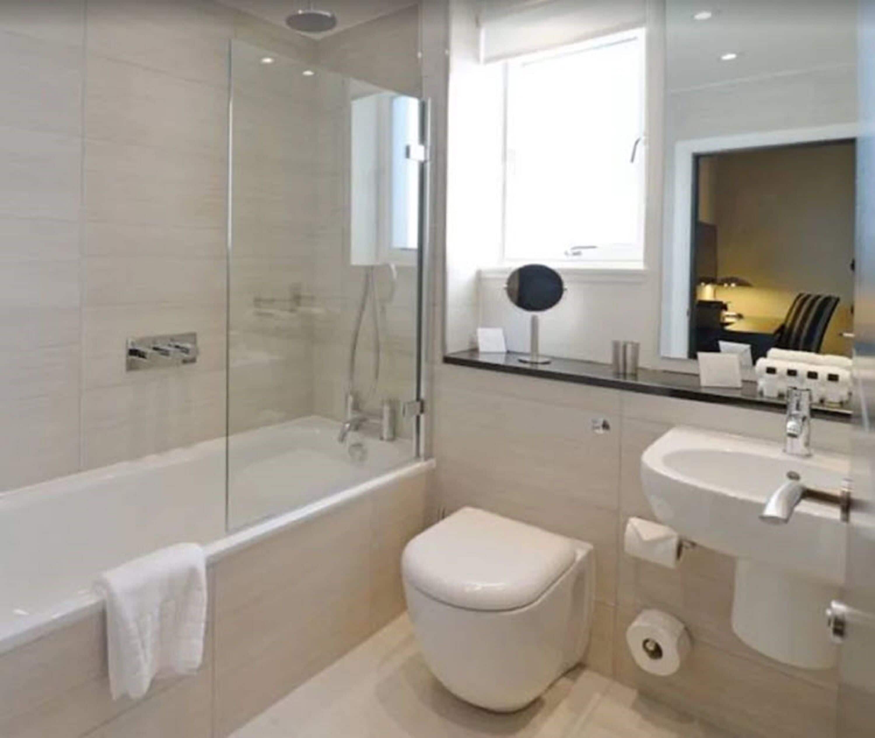 Un baño moderno con ducha de vidrio, inodoro blanco y lavamanos con espejo.