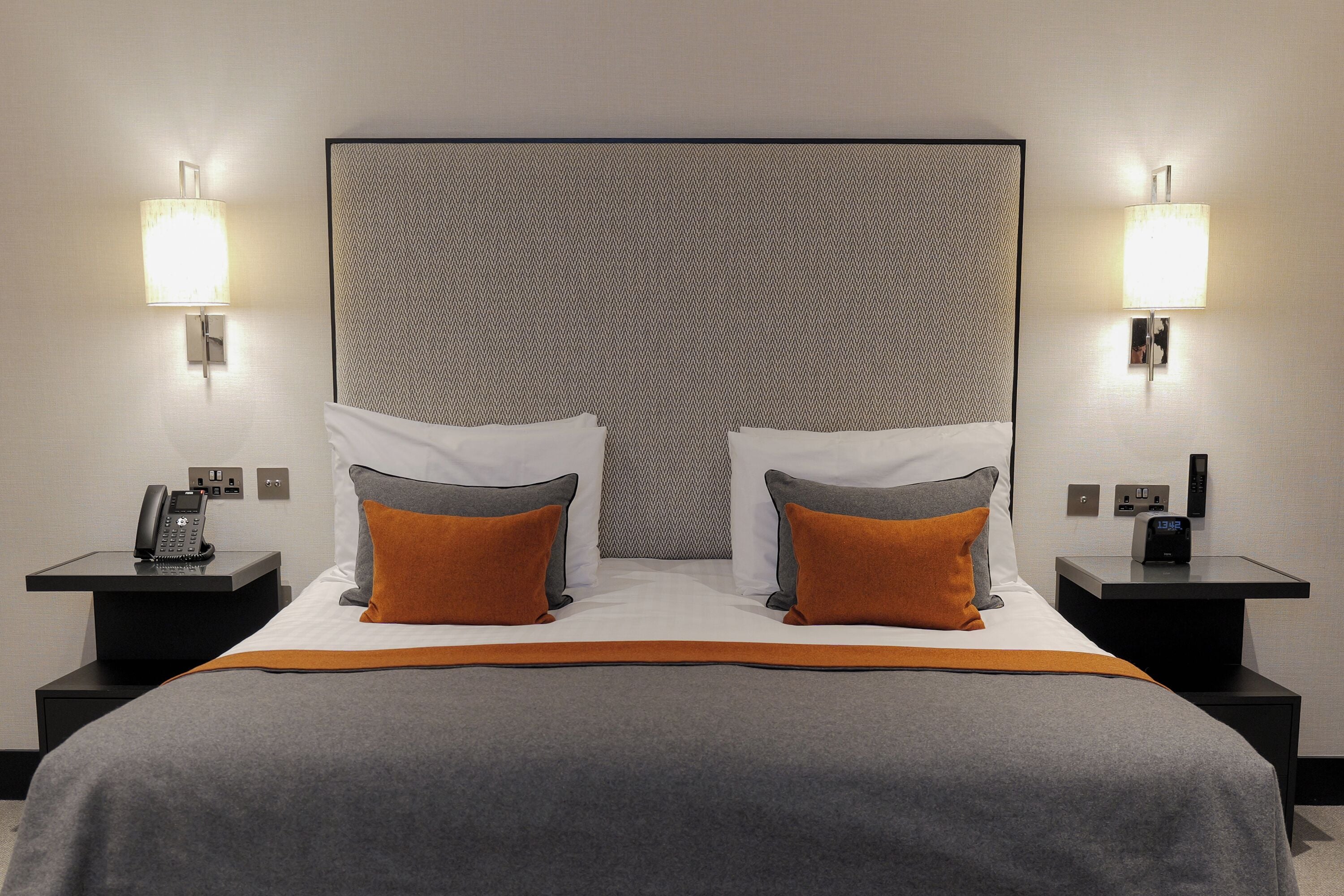 A hotel room with a large bed, two nightstands, a telephone, and a wall-mounted lamp.