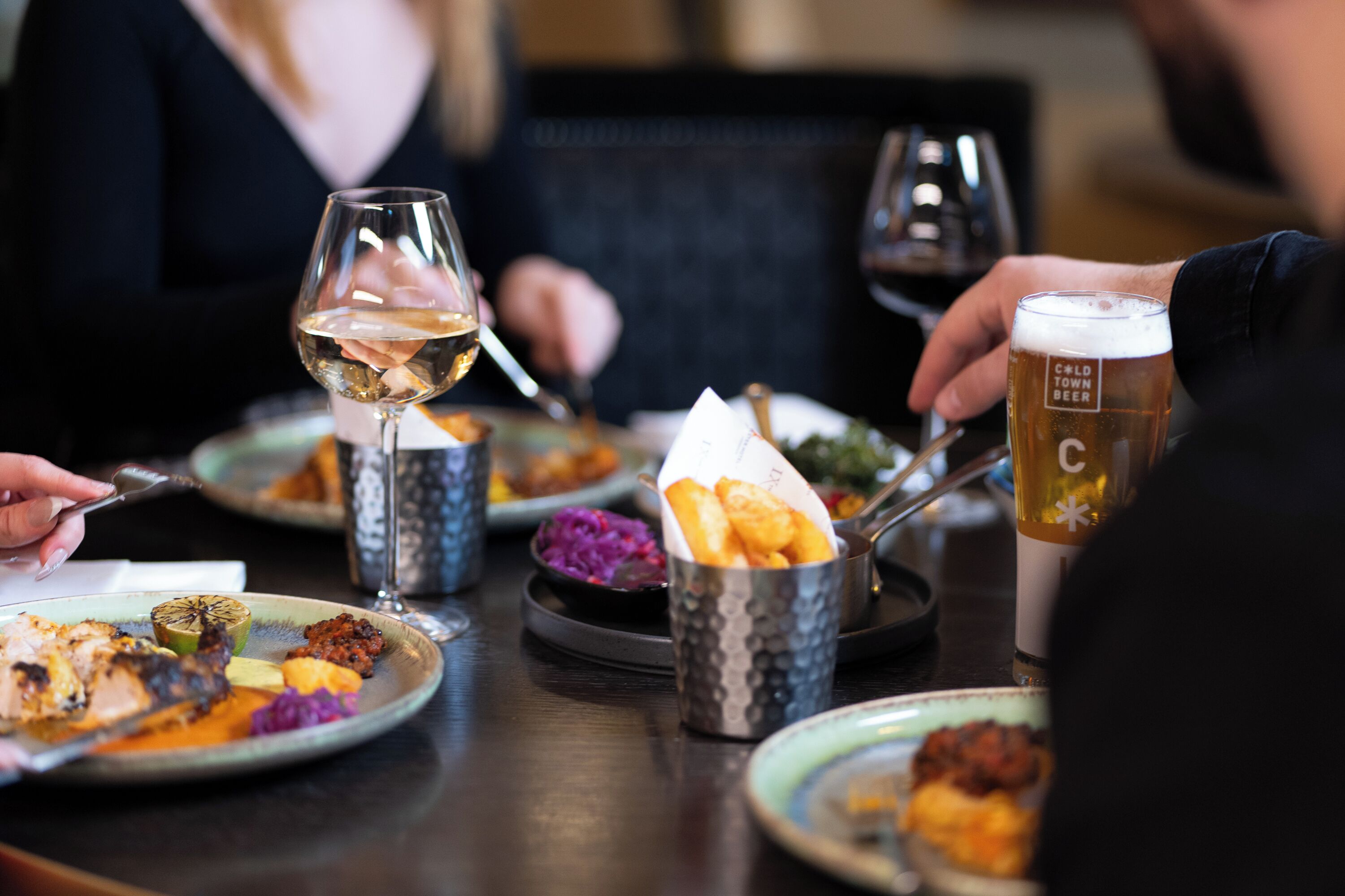Une table à manger avec des assiettes remplies de nourriture, des verres de vin et une chope de bière.