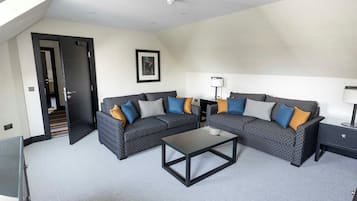 A modern living room with two patterned sofas, a glass coffee table, a side table with a lamp, and a framed picture on the wall.