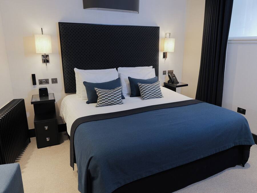 A hotel room with a large bed, two bedside tables, a headboard, and a window with curtains.