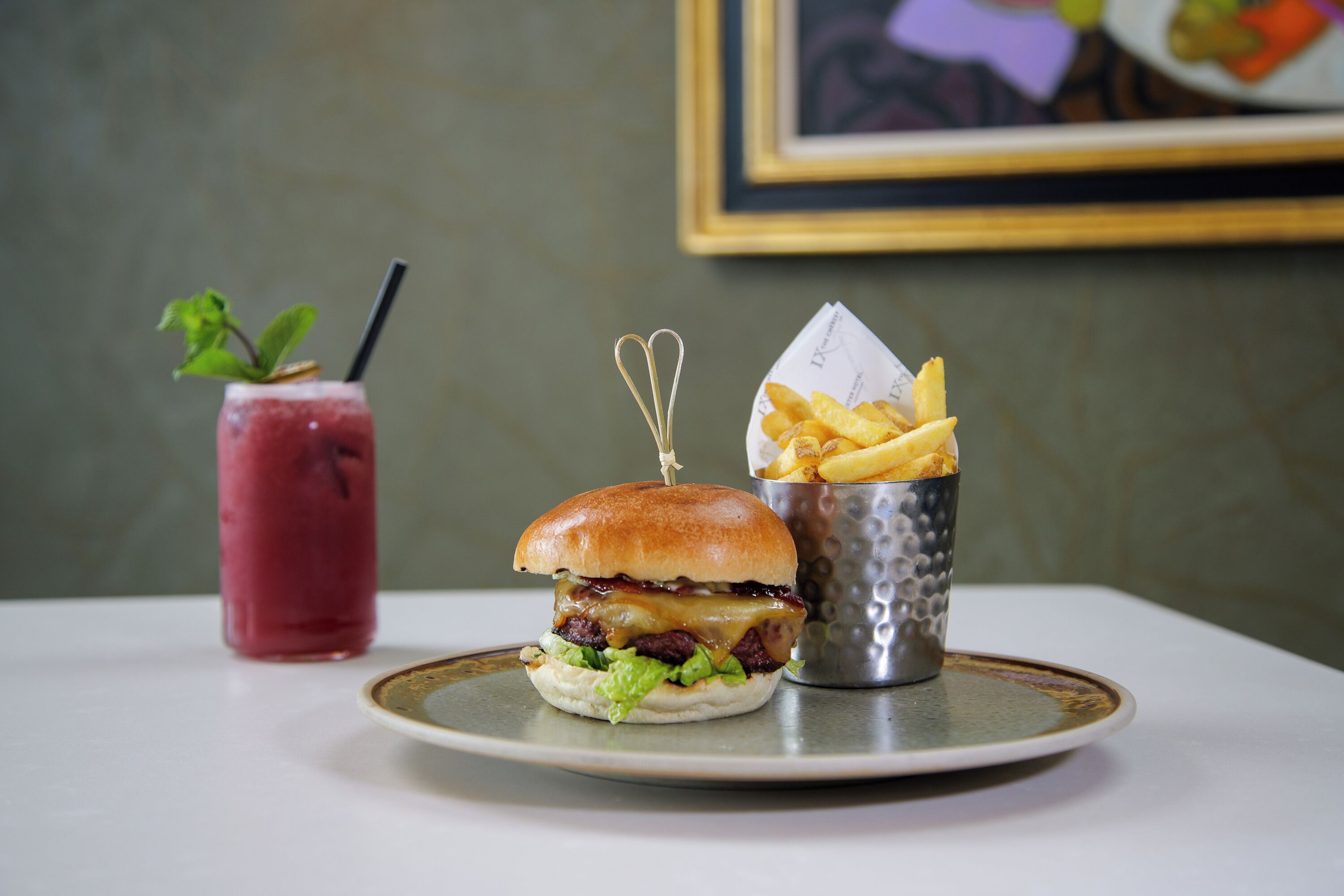 A burger with fries and a drink on a plate.