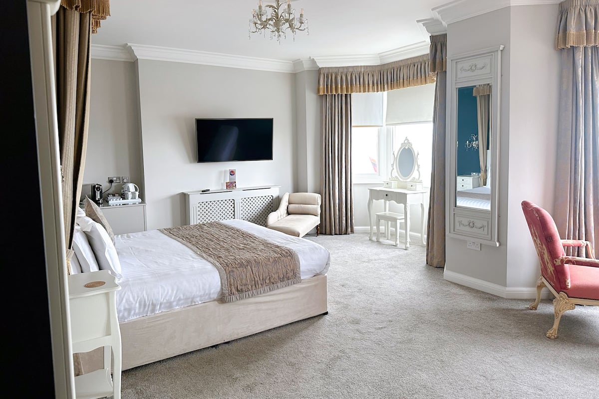 A hotel room with a large bed, a desk, a chair, a television, and a window with curtains.