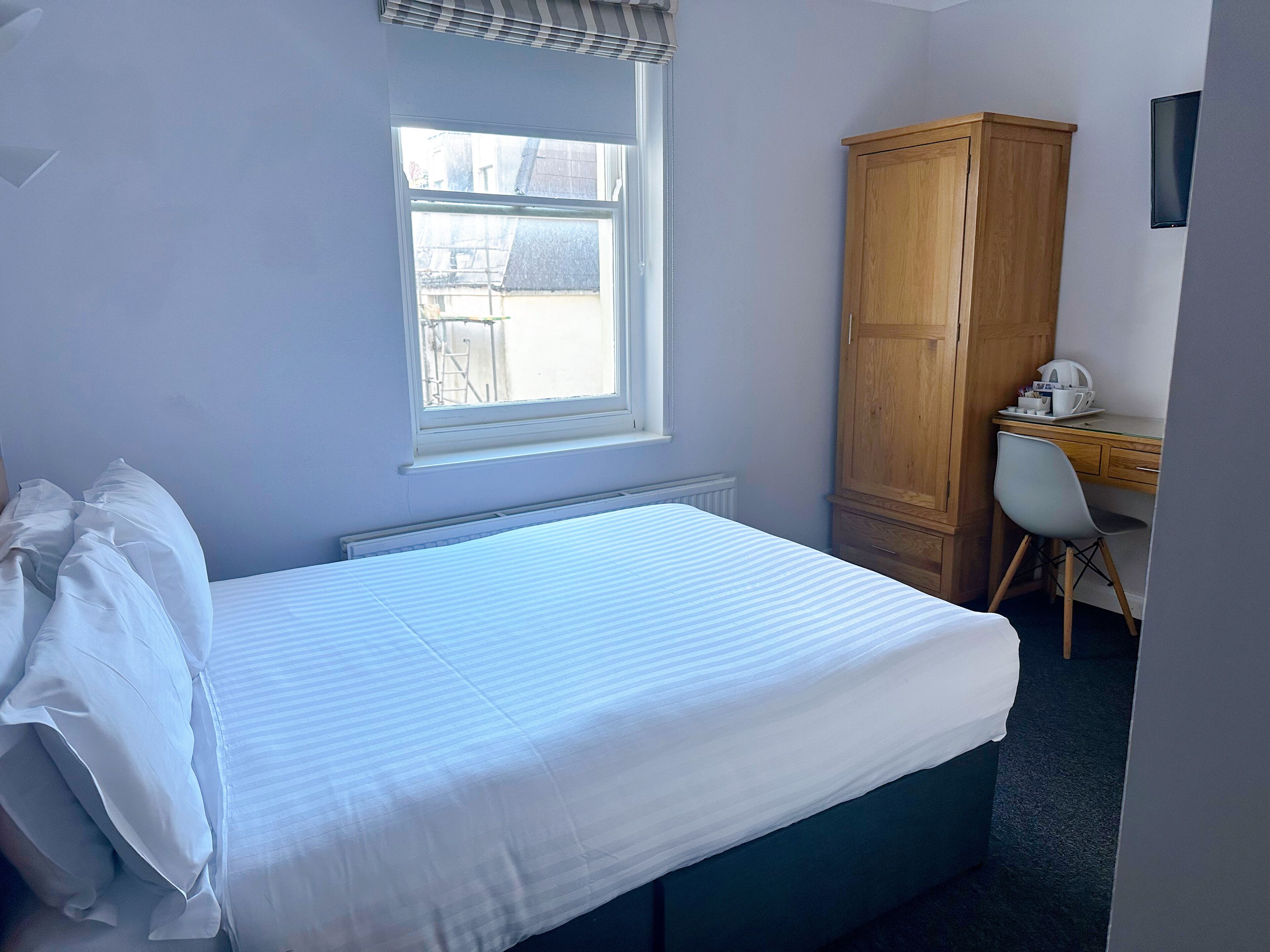 A bedroom with a bed, a window, a desk, and a wardrobe.