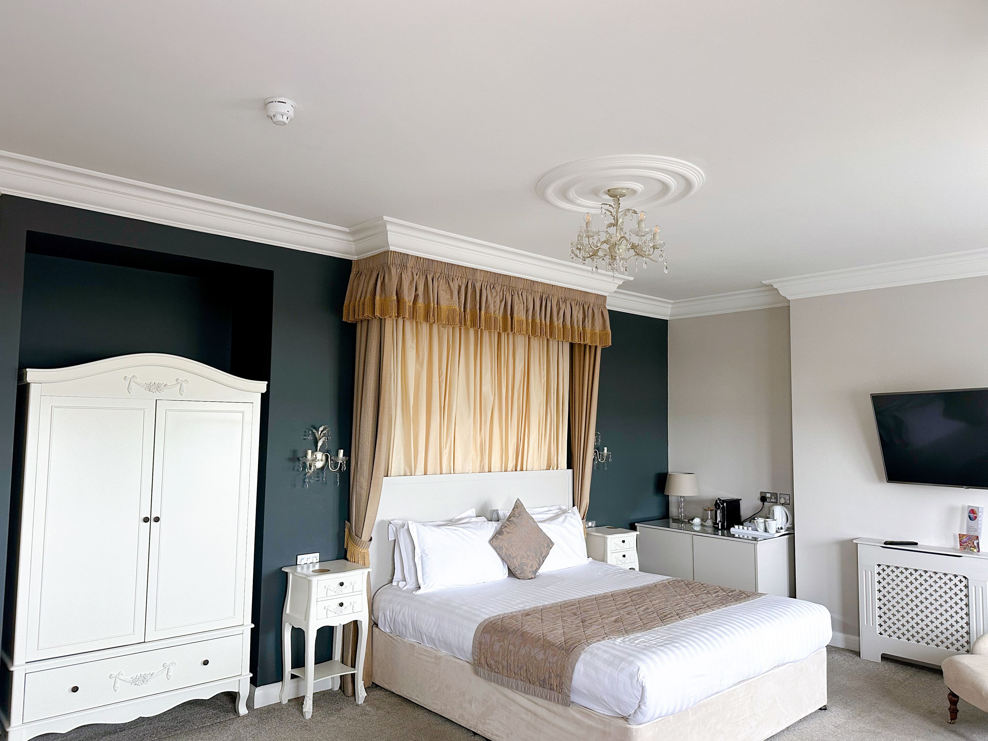 A neatly arranged bedroom with a bed, bedside tables, a wardrobe, a television, and a chandelier.