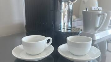 A coffee maker on a table with two white cups and saucers.