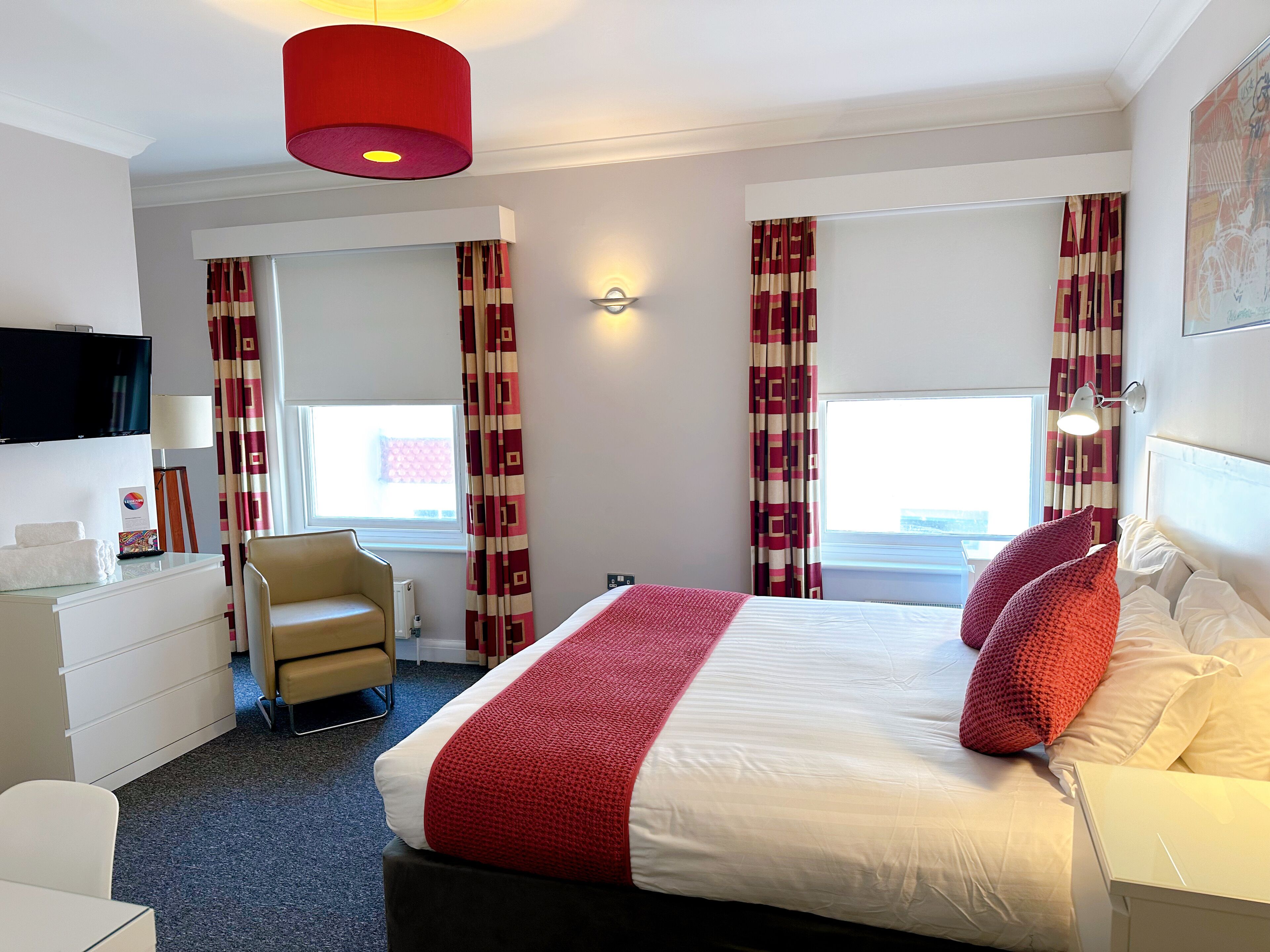 A hotel room with a bed, a desk, a chair, a TV, and curtains.