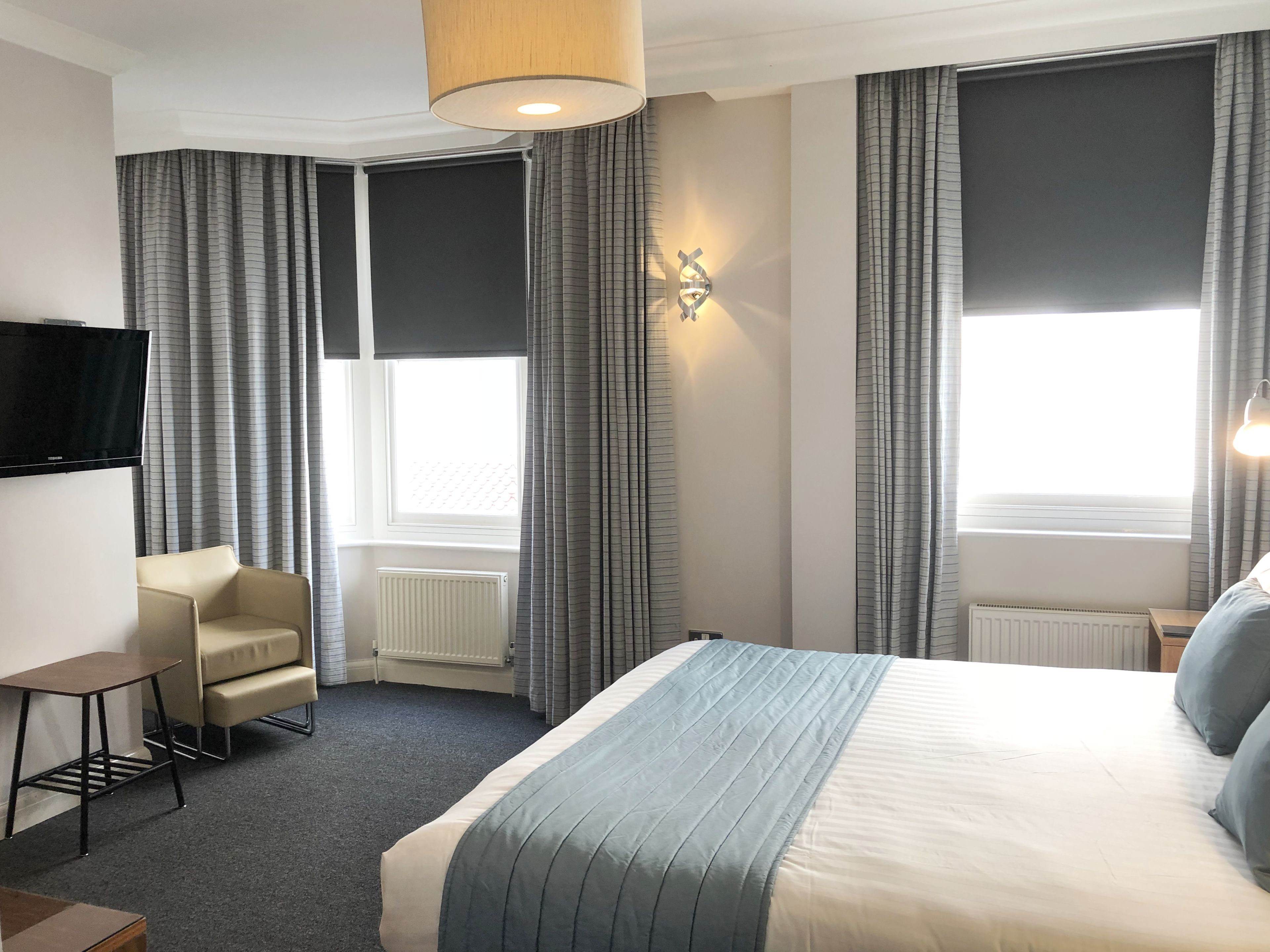 A hotel room with a bed, a chair, a TV, and a window with curtains.