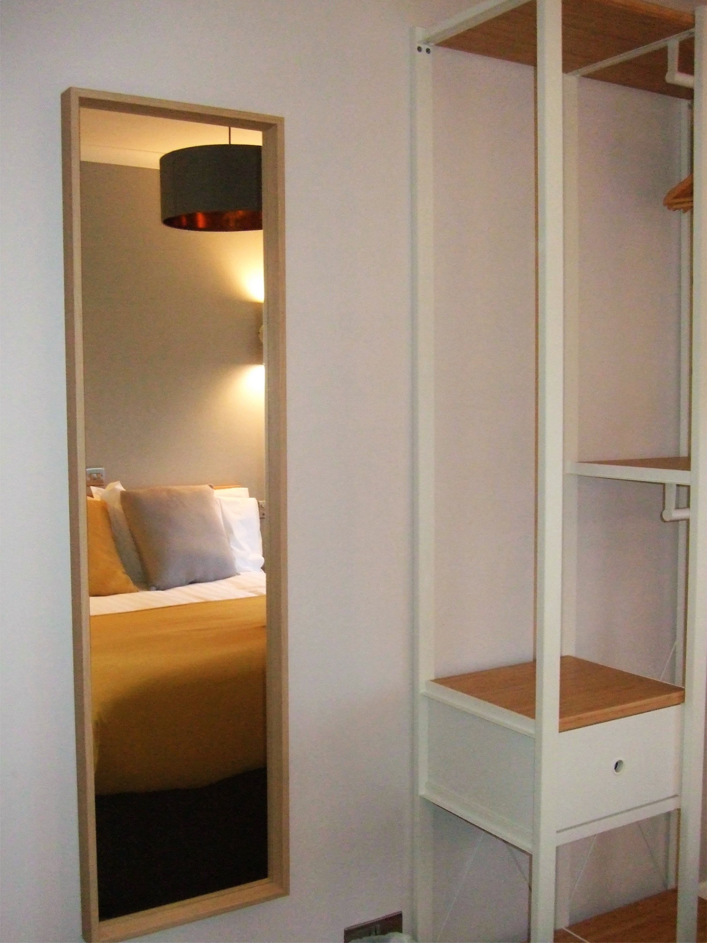 A room with a bed, a mirror, and a white shelving unit.