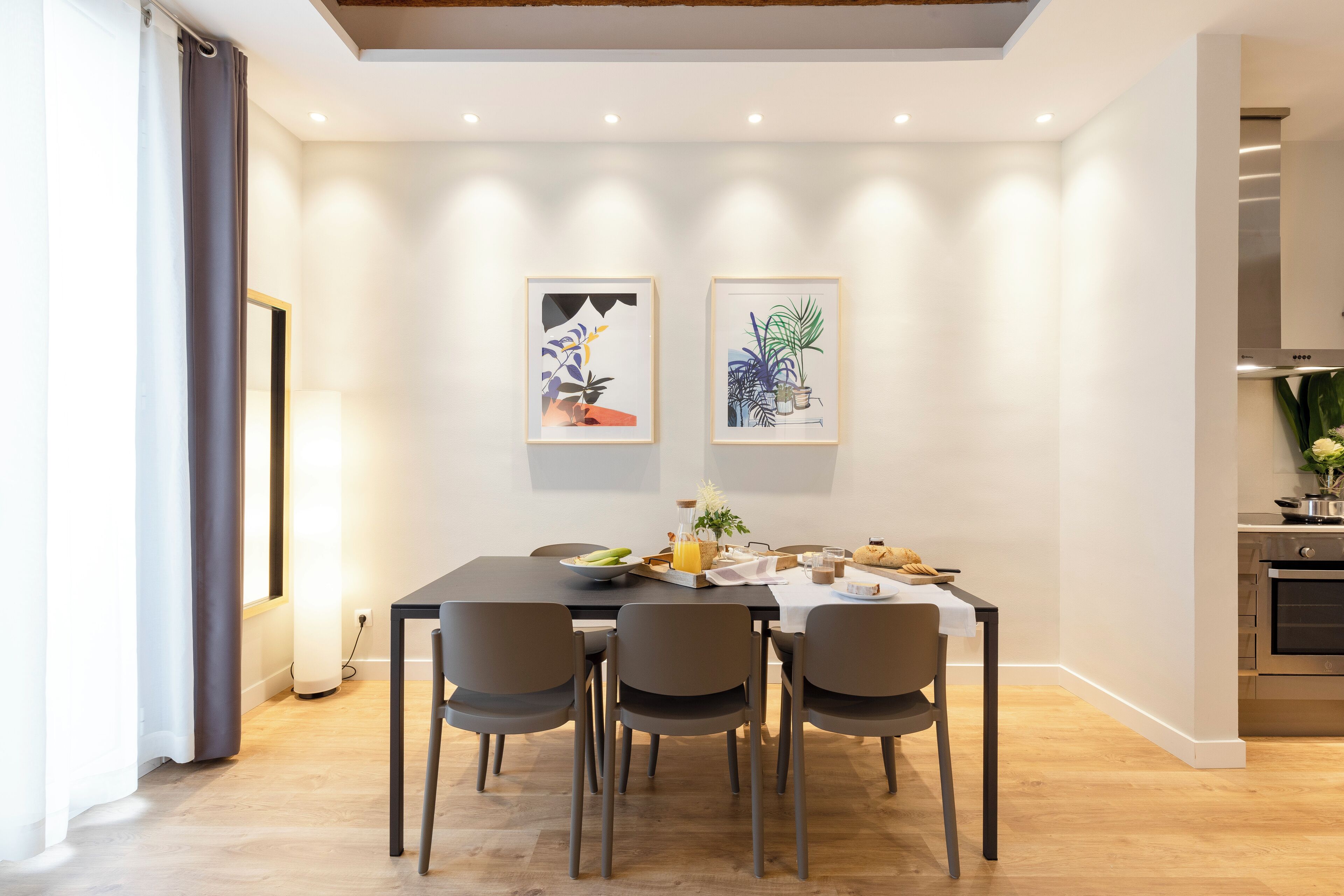 A modern dining area with a wooden table, four chairs, and two framed artworks on the wall.