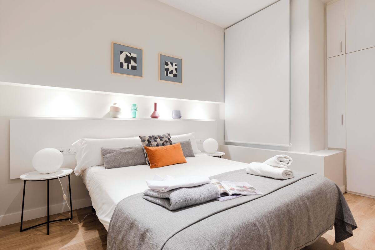 Una habitación de hotel moderna con una cama bien hecha, mesitas de noche y una obra de arte en la pared.