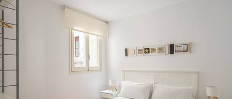 Une chambre à coucher au style minimaliste, avec un lit, des tables de chevet, une fenêtre et des éléments décoratifs sur les murs.