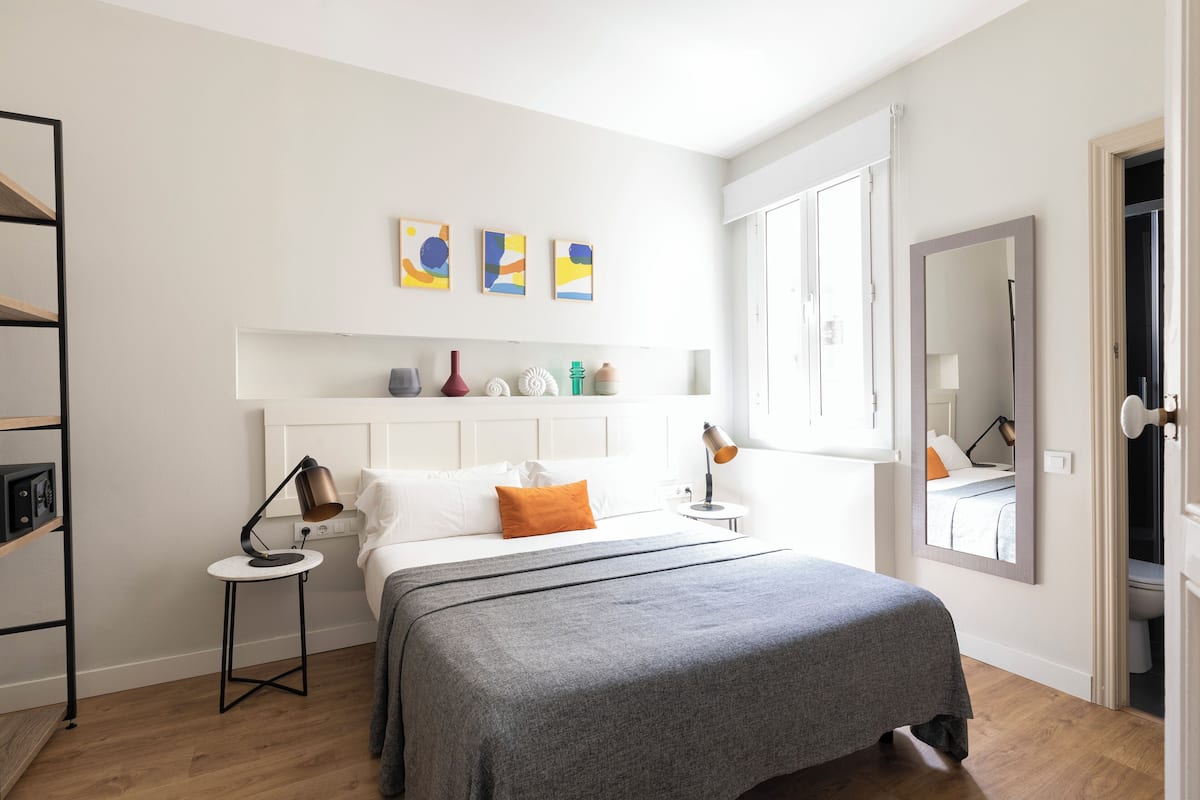 Un dormitorio moderno con cama, mesitas de noche, armario y una obra de arte en la pared.