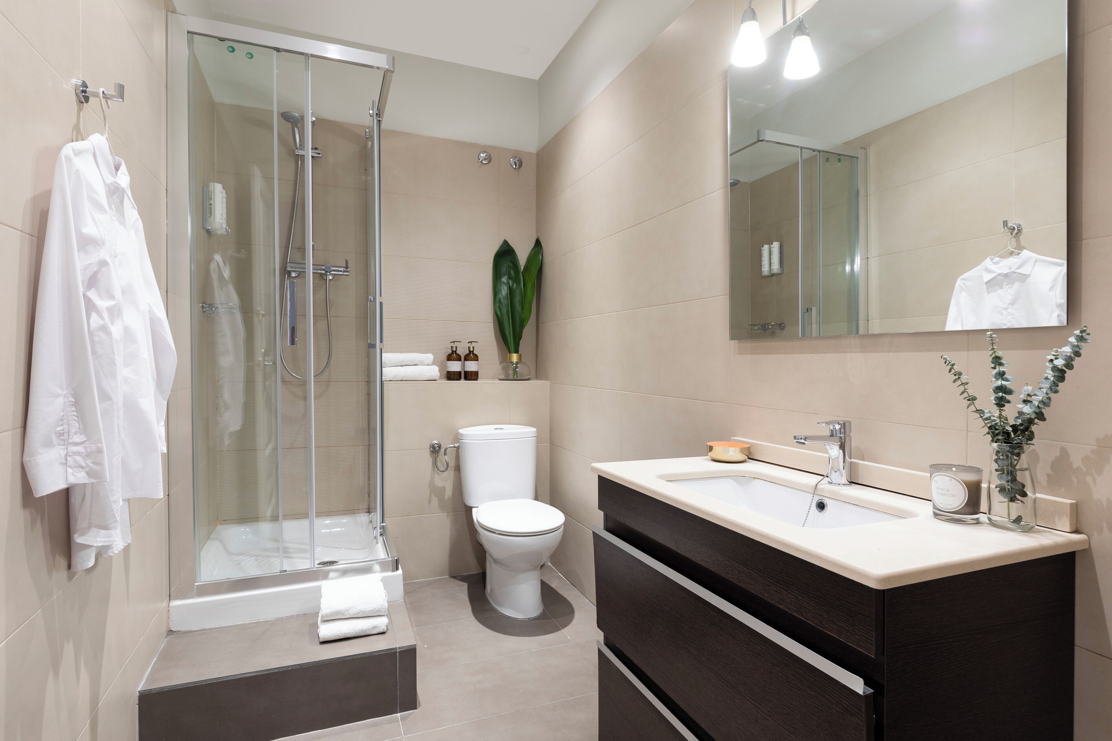 A modern bathroom with a glass-enclosed shower, a white toilet, and a vanity with a mirror.