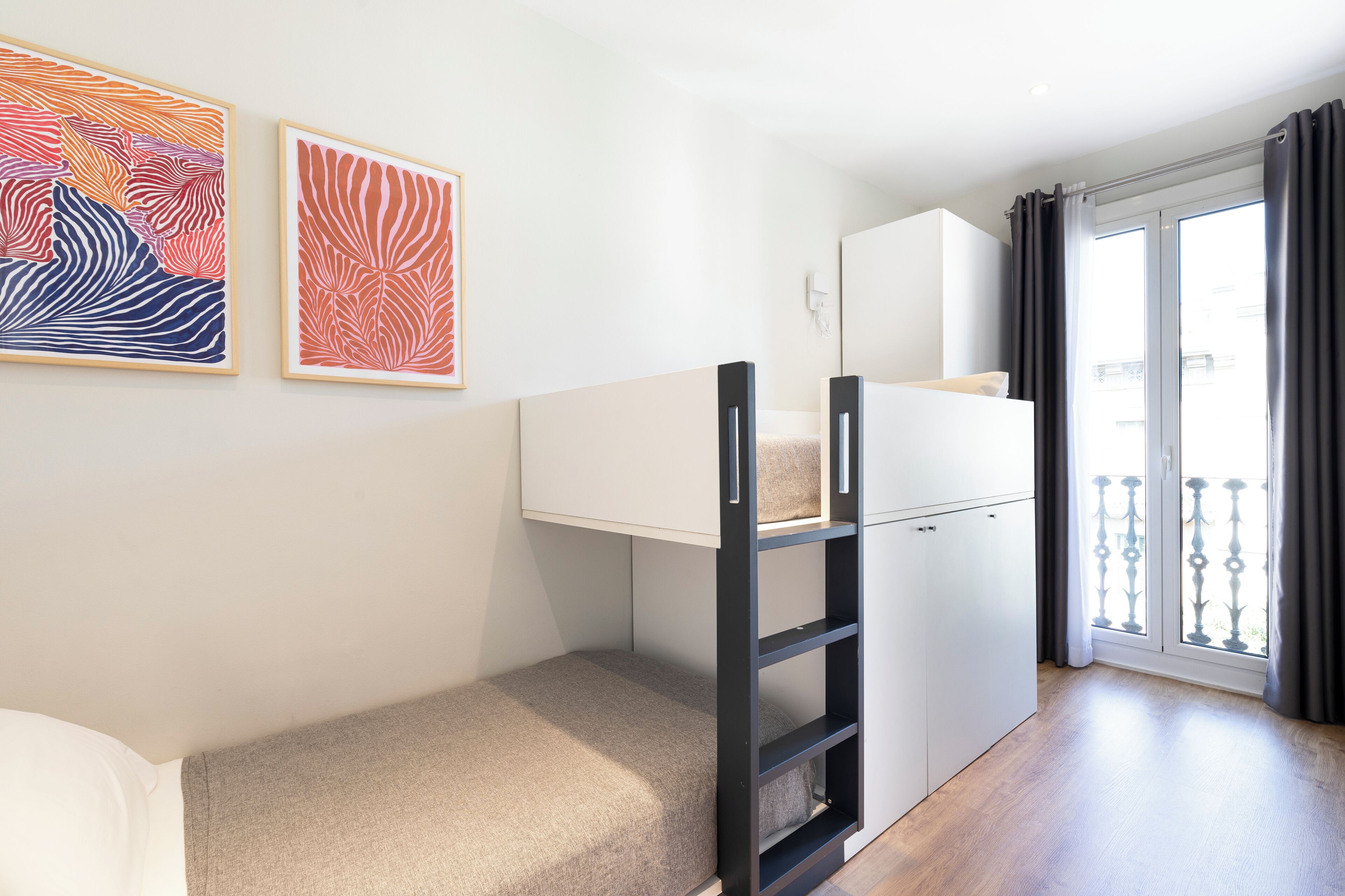 A modern, compact room with a bunk bed, a small desk, and a balcony with a view.