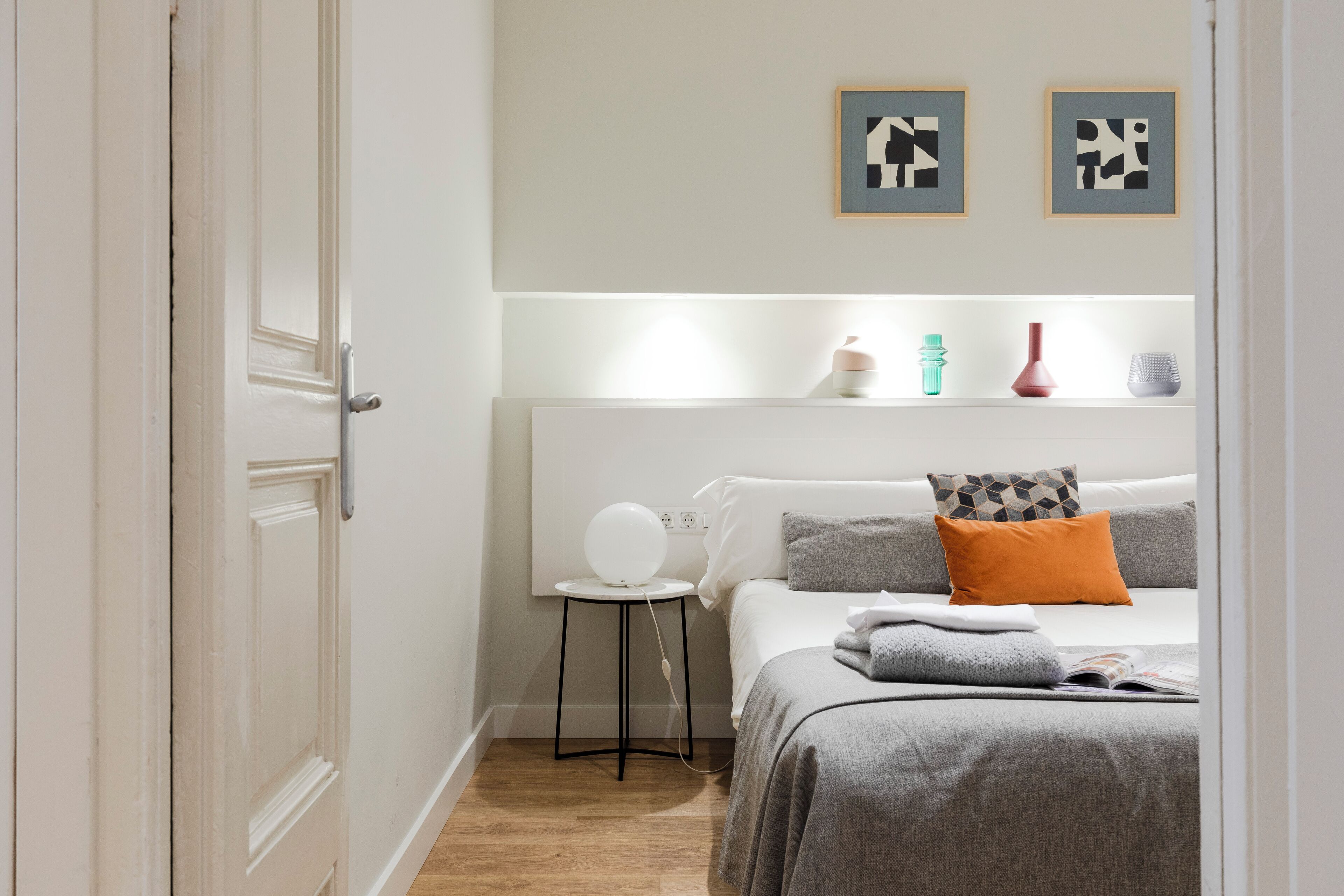 Un dormitorio con cama, mesita de noche y estante en la pared con objetos decorativos.
